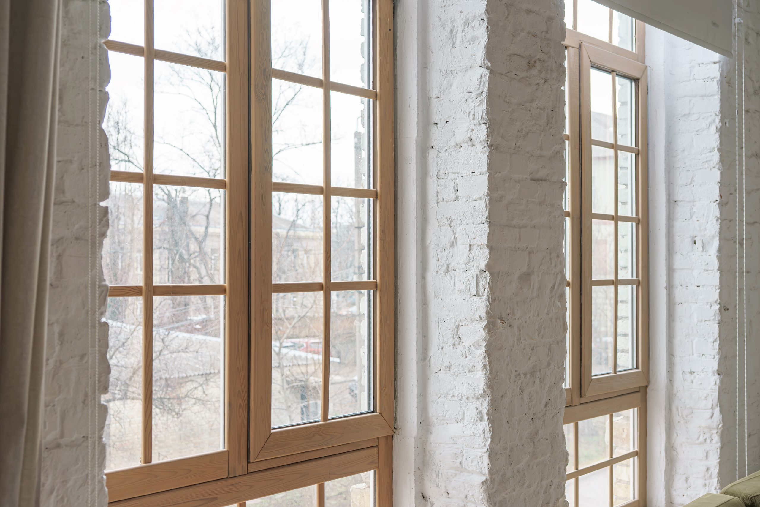 Large windows with wooden frames in loft interior with white brick walls inside modern apartment or house. Interior detail, architecture element, urban design